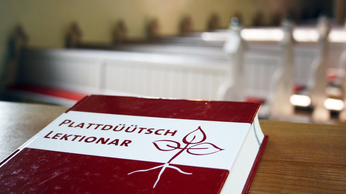 Das Buch mit dem Titel "Plattdüütsch Lektionar" auf der Ablage einer Kirchenbank.