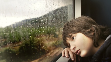 Ein kleiner Junge schaut aus dem Fenster an dem sich Regentropfen befinden