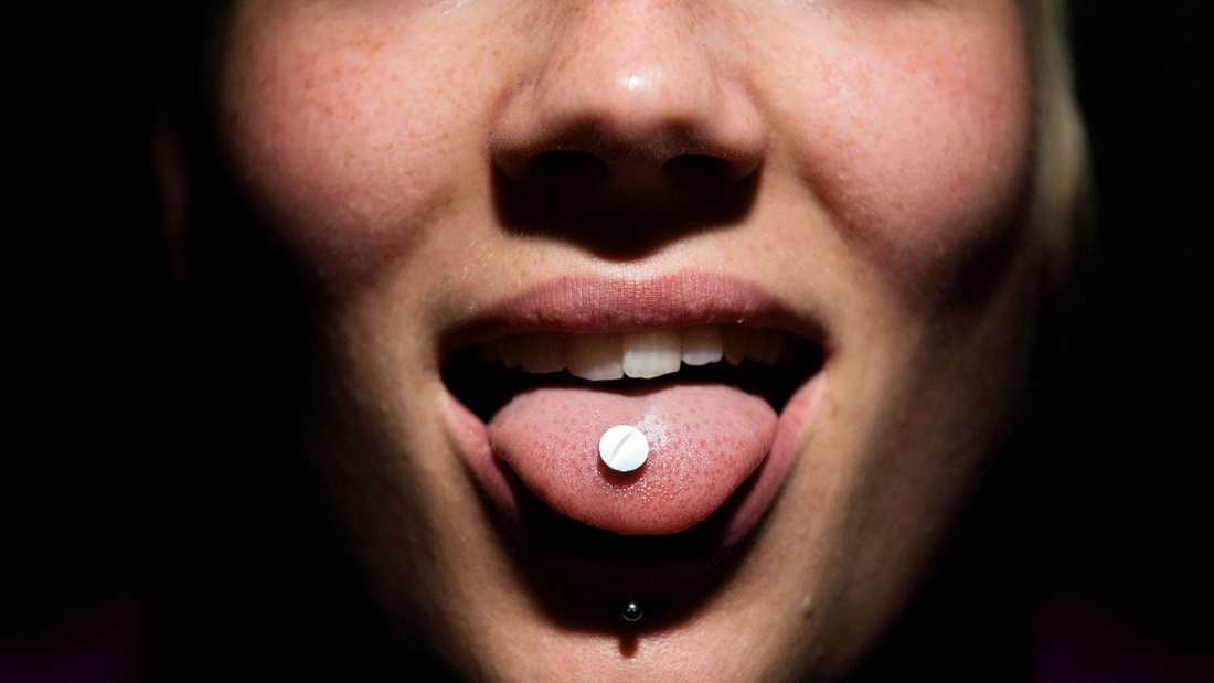 Eine Person streckt ihre Zunge heraus, auf der eine Pille liegt