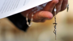 Ein Priester hält einen Rosenkranz und ein Schreiben in der Hand.
