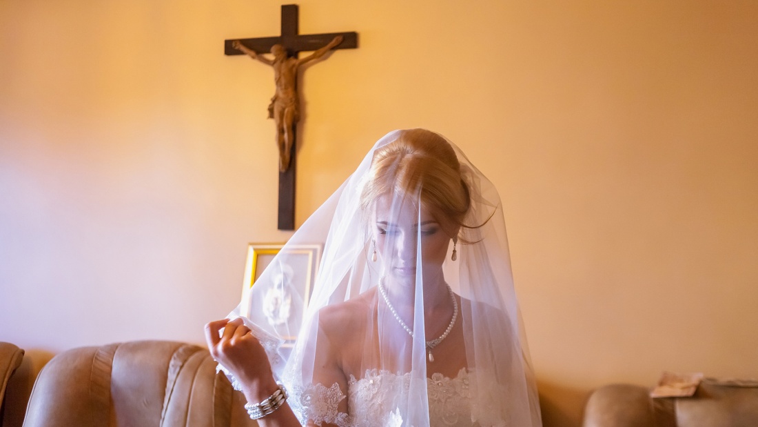 Braut mit Schleier steht vor Kreuz