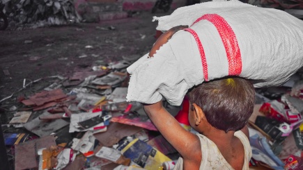 Kind auf einem Müllberg mit einem schweren Leinensack auf dem Rücken