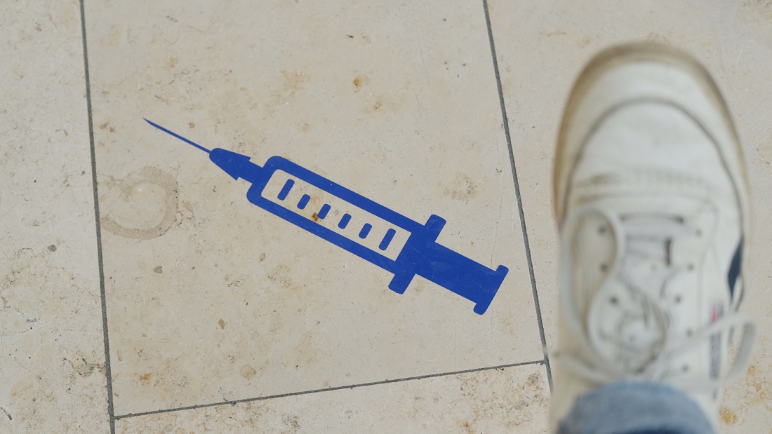 Aufkleber einer Spritze ist auf dem Boden eines Impfzentrums aufgeklebt