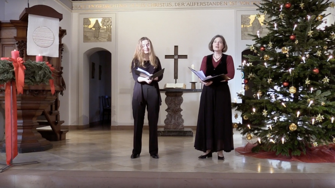 Screenshot aus dem Video mit zwei singenden Damen vor dem Altar mit Weihnachtsbaum