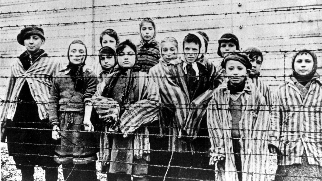 Kinder hinter einem Stacheldraht des Konzentrationslagers Auschwitz-Birkenau, welches das zentrale Symbol für den Völkermord an den Jüdinnen und Juden und die deutschen Gräueltaten in der NS-Zeit ist. 