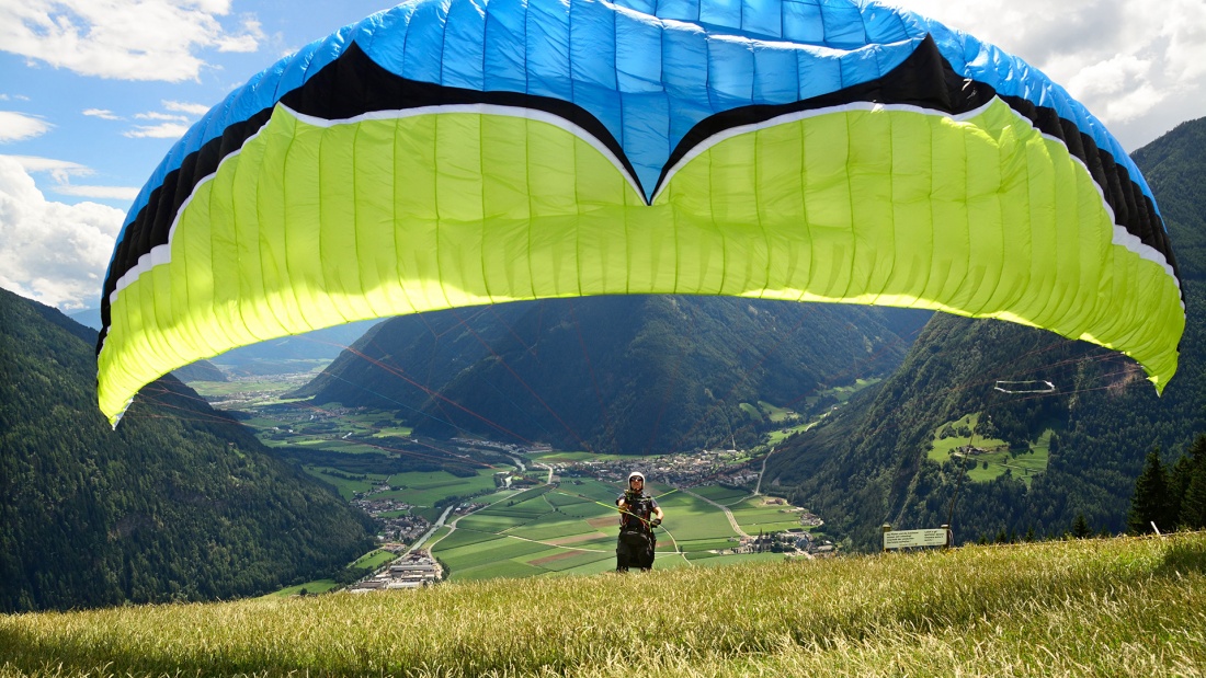 Ein Paraglideschirm-Flieger beim Start mit Bergen im Hintergrund