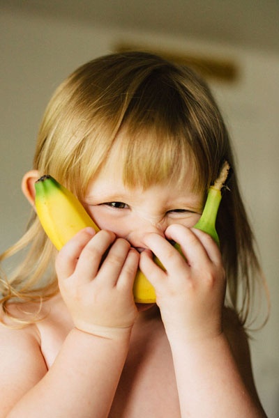 Ein Mädchen hält sich eine Banane vors Gesicht.