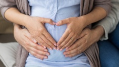 Mann und Frau halten Hände auf ihren schwangeren Bauch