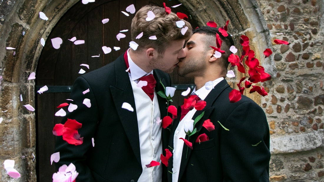Homosexuelles Hochzeitspaar küsst sich vor einer Kirche