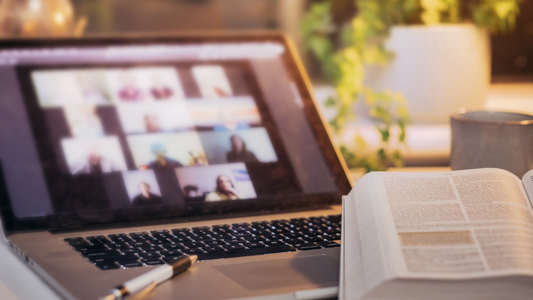 Laptop, auf dem ein online-Meeting stattfindet, mit aufgeschlagener Bibel