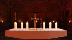 Ein bronzenes Kreuz steht zwischen sechs Kerzen auf einem Altar. 