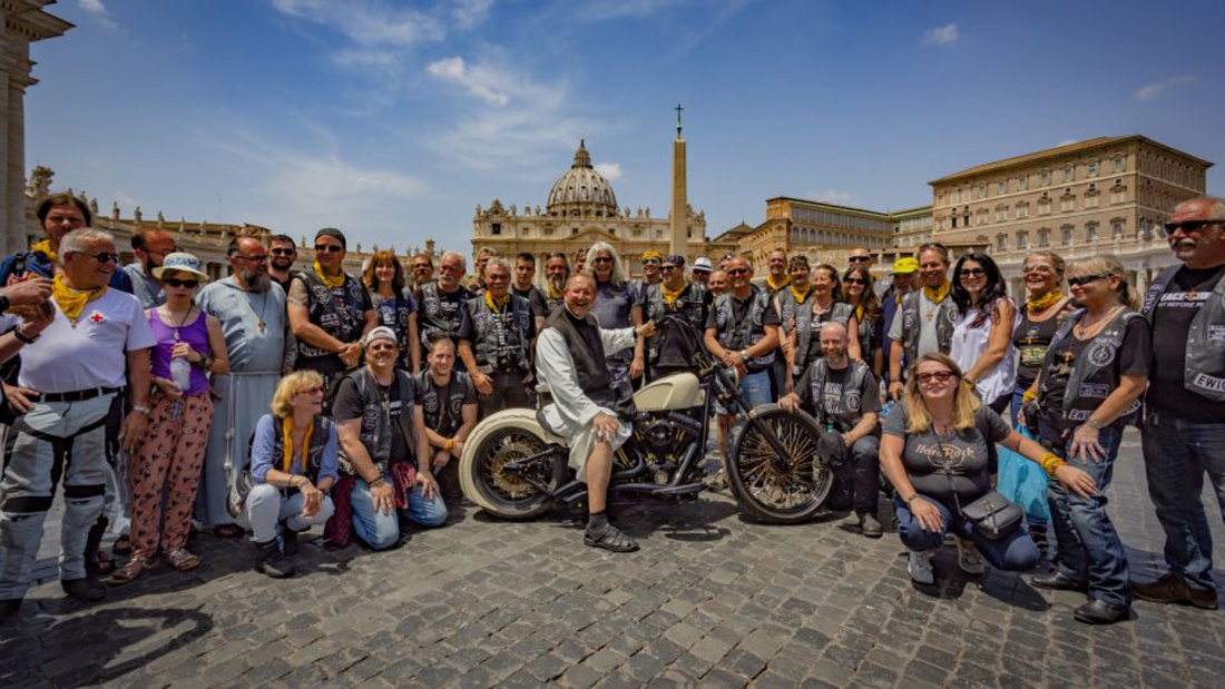 Eine Gruppe Motoraradfahrer steht auf dem Petersplatz in Rom. Einer sitzt auf einer weißen Harley Davidson. 