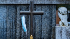 Medizinische Maske hängt an einem steinernen Kreuz auf einem Grabstein.