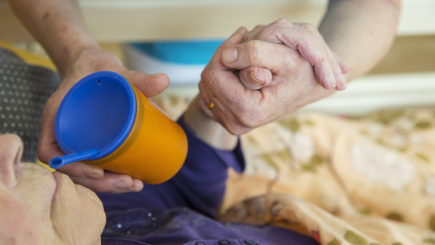 Pflegerin hilft einer Bewohnerin beim Trinken in einem Altenheim