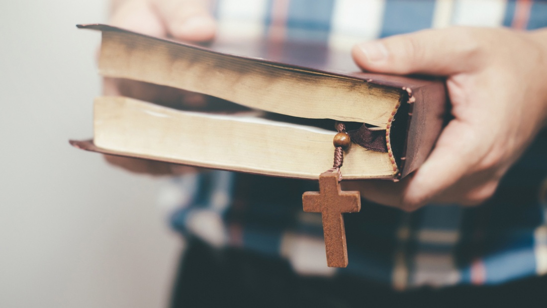 Junger Mann mit Bibel und Kreuz in der Hand
