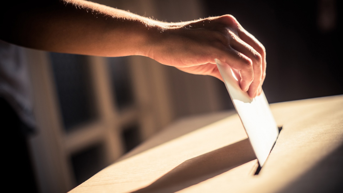 Hand wirft Umschlag mit Wahlzettel in eine Wahlurne