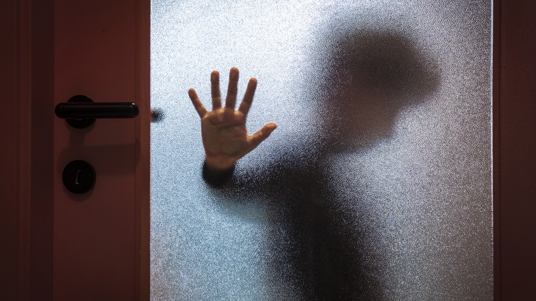 anonymer kleiner Junge hinter einer Glastür mit Hand gegen die Tür