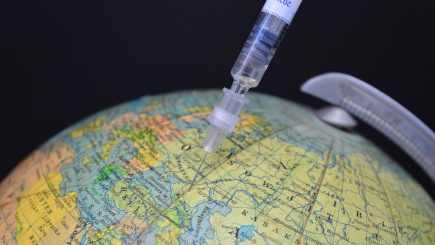 Eine Impfspritze markiert irgendeinen zufälligen Ort auf einem Globus