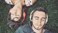 Mann und Frau liegen auf einer Wiese und hören über Kopfhörer Musik.