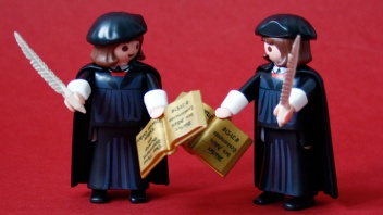 Eine Playmobil-Figur von Martin Luther mit dem Federkiel in rechten Hand steht einer Playmobil-Figur von Martin Luther mit dem Federkiel in der linken Hand gegenüber.