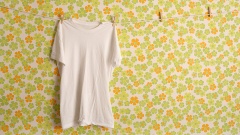 Ein weißes T-Shirt hängt vor einer Wand mit Blümchentapete auf einer Wäscheleine.