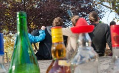 Alkoholflaschen im Vordergrund, Jugendliche von hinten zu sehen, im Hintergrund.
