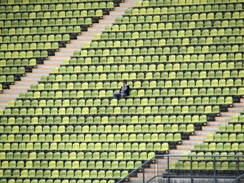Ein junger Mann sitzt alleine in einem Sportstadion.