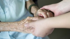 Pfleger reicht einer älteren Frau die Hände.