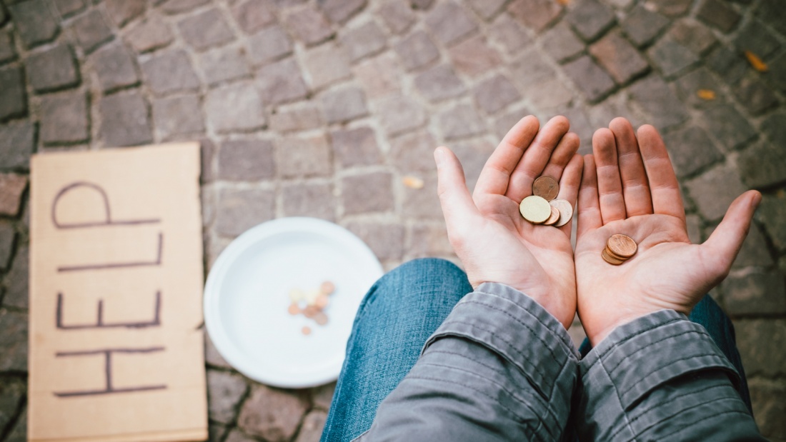 Ausschnitt von einem Bettler mit aufgehaltenen Händen mit Münzen und einem "Help"-Schild
