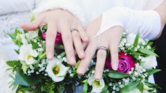 Zwei Bräute halten ihre Hände mit Eheringen über ihren Brautsträußen.