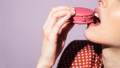 Eine Frau isst ein pinkes Macaron.