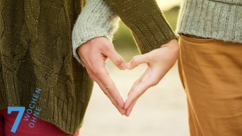 Ein Mann und eine Frau stehen nebeneinander und formen mit ihren Händen ein Herz zwischen sich.