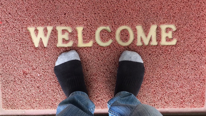 Ein Mann steht in Strümpfen auf einer Fußmatte, auf der das Wort "Welcome" steht.