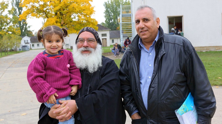 Bischof Anba Damian von der koptisch-orthodoxen Kirche in Deutschland mit Diplom-Ingenieur Muhammad Rodan und dessen Tochter Badran (3) in der Flüchtlingsunterkunft in Borgentreich.