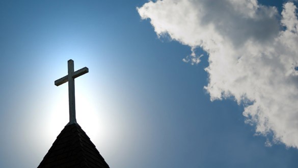 Kirchturm mit Kreuz vor blauem Himmel
