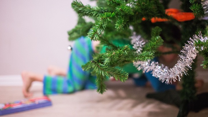 Ein Kind sucht unter dem Weihnachtsbaum nach Geschenken.