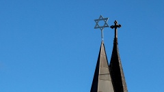 Turmdach mit Kreuz neben Turmdach mit Davidsstern vor blauem Himmel