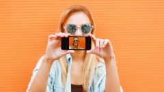 Eine Frau macht ein Selfie vor einer orangenen Wand.