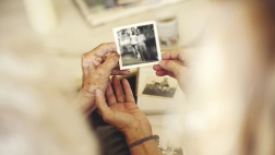 Eine alte und eine junge Frau schauen sich alte Schwarz-Weiß-Fotos zusammen an.